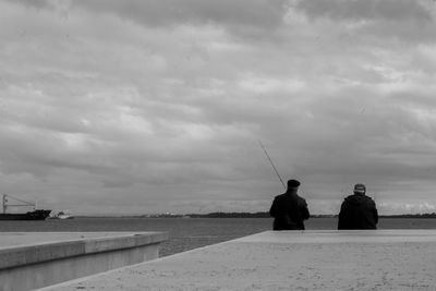 Rear view of men fishing in sea against sky