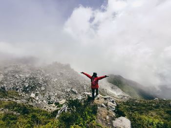 Rear view of woman jumping on mountain against sky