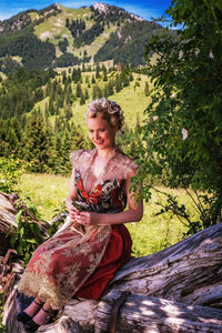 Portrait of romantic woman in dirndl with elaborate hairstyle holding flower in hand