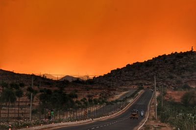 Vehicles on road by mountains against clear sky at sunset