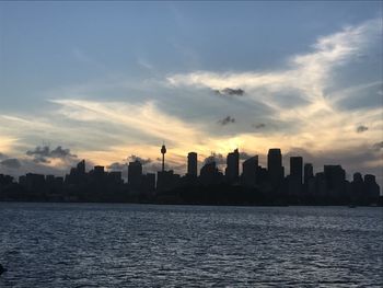 Sea by cityscape against sky during sunset