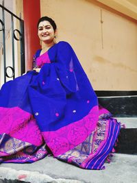 Low angle portrait of smiling young woman wearing sari sitting on steps