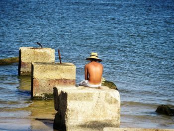 Rear view of man sitting on wall by sea