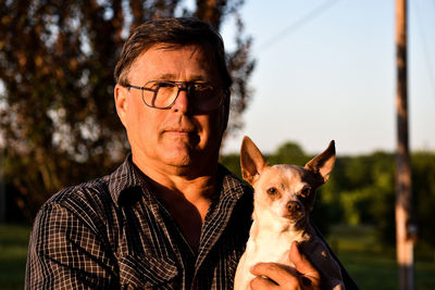 Portrait of man holding dog against sky