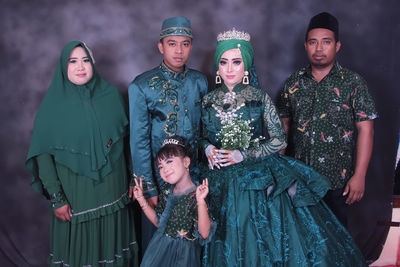 Portrait of newlywed couple with family standing against curtain