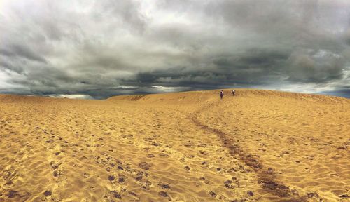 Scenic view of arid landscape against cloudy sky