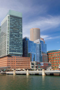 Modern buildings by river against sky in city