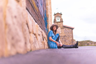 Full length portrait of woman sitting on land against wall