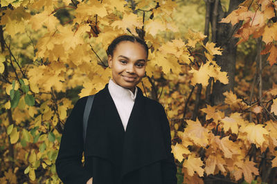 Portrait of smiling young woman standing by leaves during autumn
