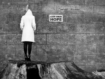 Rear view of woman standing on tree stump against wall with text