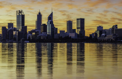 Sea by modern buildings against sky during sunset