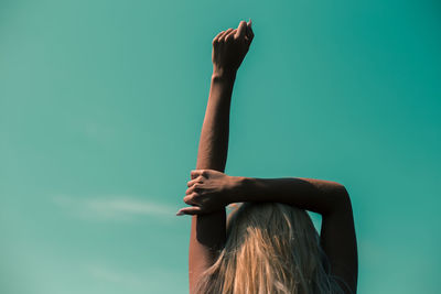 Rear view of woman with hand raised standing against blue sky