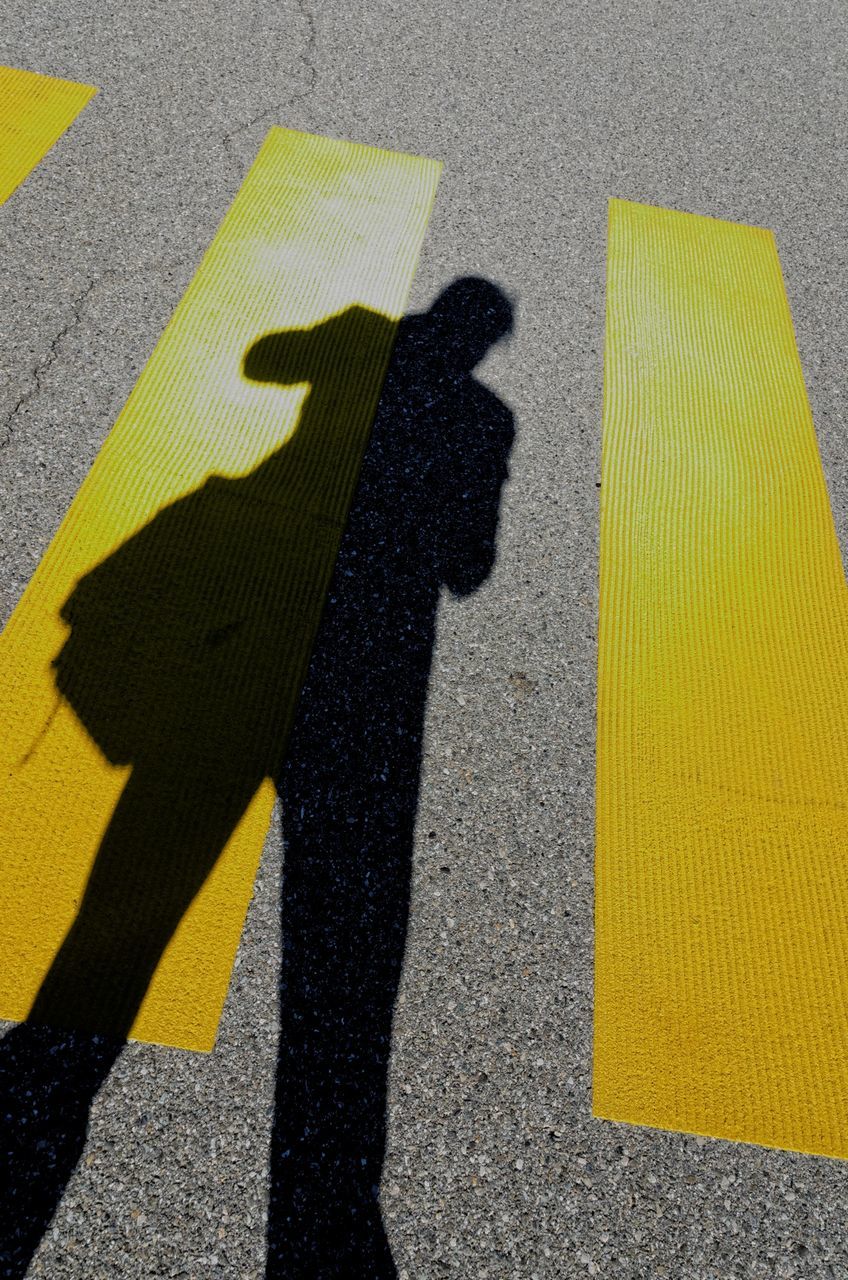 yellow, high angle view, street, road marking, shadow, asphalt, road, focus on shadow, sunlight, guidance, day, outdoors, arrow symbol, transportation, zebra crossing, textured, communication, directional sign, direction, elevated view