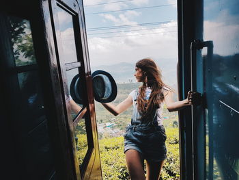 Woman looking outside while standing on train doorway
