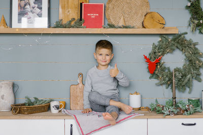 Beautiful baby boy sits on the kitchen table and shows good with his thumb