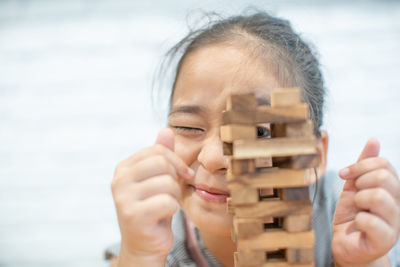 Close-up portrait of girl playing block removal game against wall