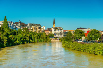 Buildings by river against clear blue sky