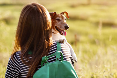 A dark-haired girl with a green backpack on her back and a striped t-shirt hugs a dog 
