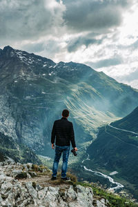 Rear view of man standing on rock against mountains