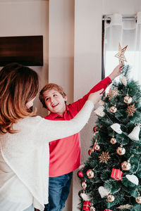 Son and mother decorating christmas tree at home