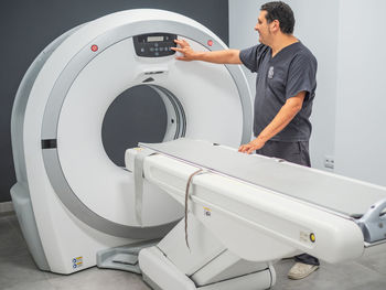Side view of adult man in scrubs pushing buttons on modern mri scanner while working in clinic