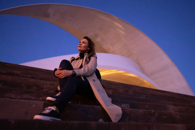 Low angle view of young woman with umbrella standing against clear sky