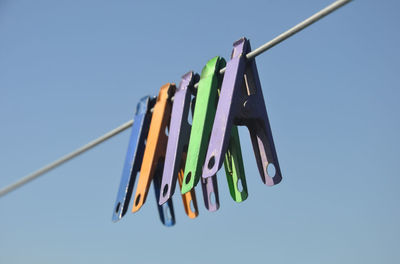 Low angle view of multi colored clothespins hanging against blue sky