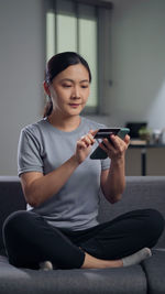 Portrait of young woman using mobile phone while sitting on sofa at home