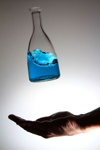 Cropped hand catching blue liquid in flask against white background