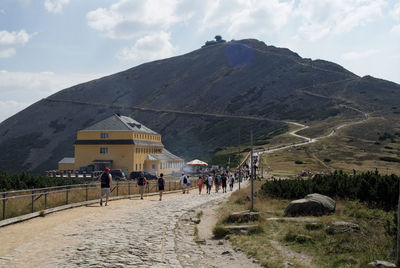 People walking on mountain against cloudy sky