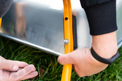 On the street, a man spins a new metal wheelbarrow for work, tightens bolts.