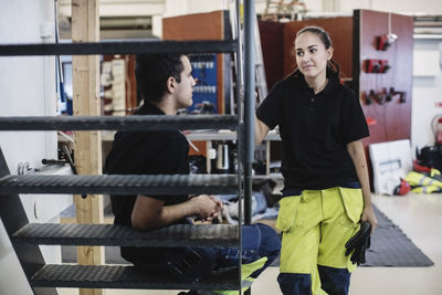 Female auto mechanic student looking at male friend at workshop