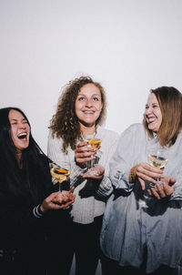 Happy young woman drinking glasses on table against wall