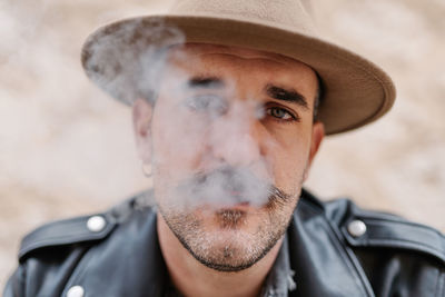 Cool handsome guy in with gorgeous mustache smoking cigarettes and looking at camera on blurred background