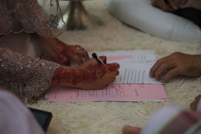 Cropped henna tattooed hand of bride signing document on rug
