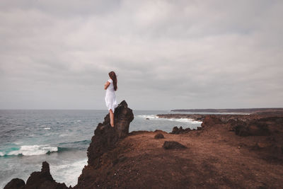 Woman standing on rock at beach against sky