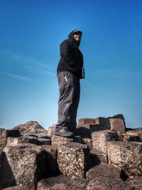 Low angle view of man standing on rocks at giants causeway against blue sky