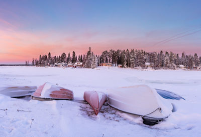 Upside down boats on snow covered field against sky during sunset