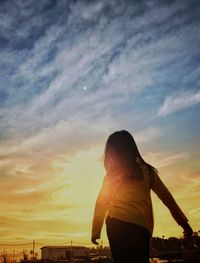 Rear view of woman standing against sky during sunset