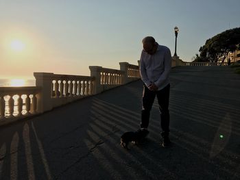 Man with dog standing against sky during sunset