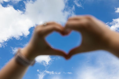 Low section of woman making heart shape against sky