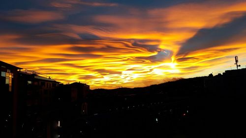 Silhouette buildings against dramatic sky during sunset