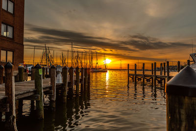 Wooden posts in sea against sky during sunset