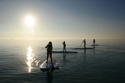 Silhouette people paddleboarding on sea against sky