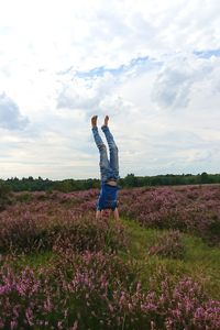 Boy doing handstand on grassy field against cloudy sky