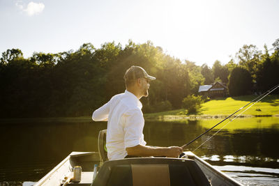 Man fishing while sitting in rowboat on lake during sunny day