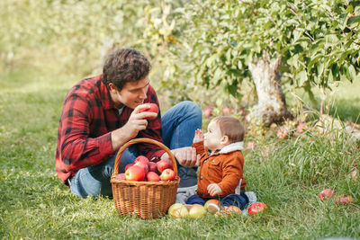 Portrait of happy father and son sitting while fruits in basket at park