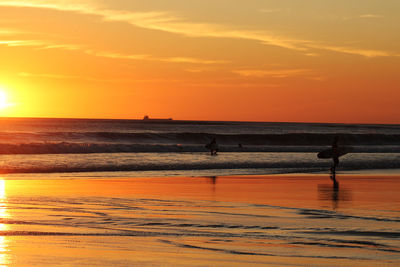 Silhouette surfers walking on the beach