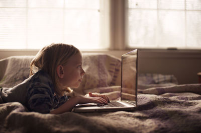 Boy using laptop while lying on bed at home