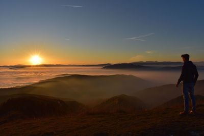 Man standing on mountain against sky during sunset